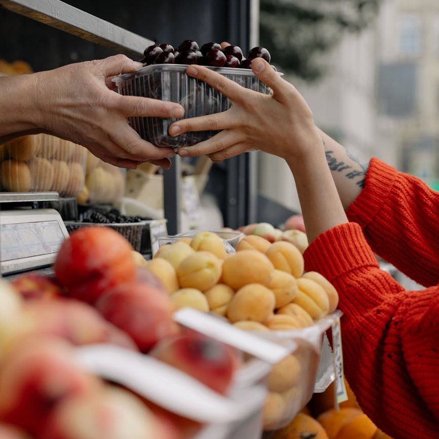 A person handing another person a basket of cherries at a fruit stand. 