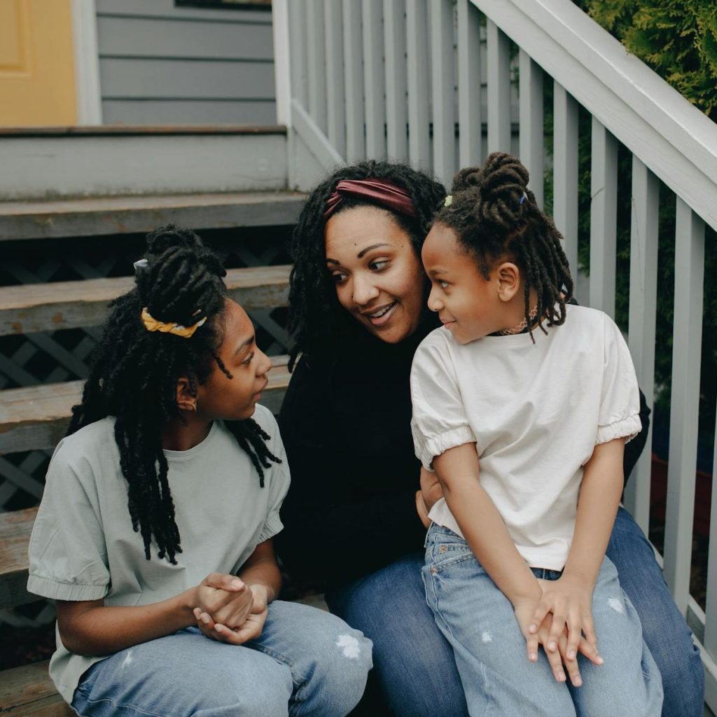 A mother and her two children sitting together on the front steps of their house. 